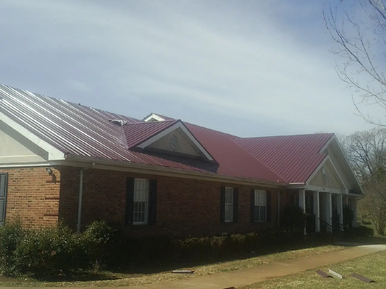 Red metal roof with gabled entries on a long brick building, from a Hail Damage Roof Repair job in Garrett