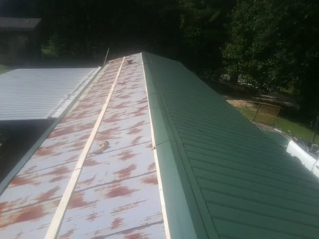 Old rusted panels beside newly installed green metal roofing — Wind Damage Roof Repair by Roofing Brothers in Garrett